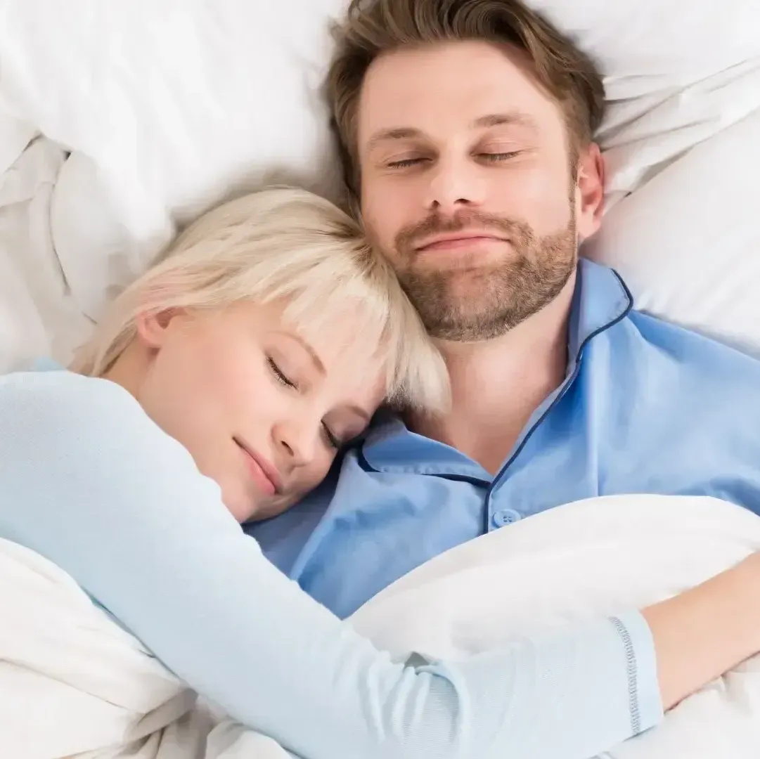 A man and a woman are sleeping in a bed with their eyes closed