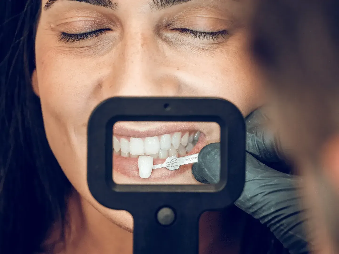 A woman is looking at her teeth through a magnifying glass.