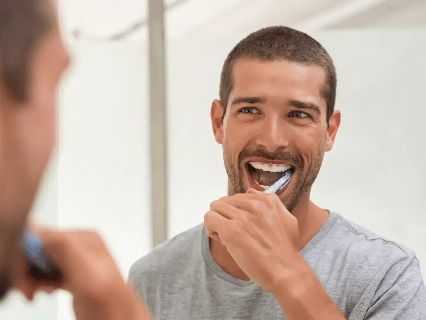 A man is brushing his teeth in front of a mirror.