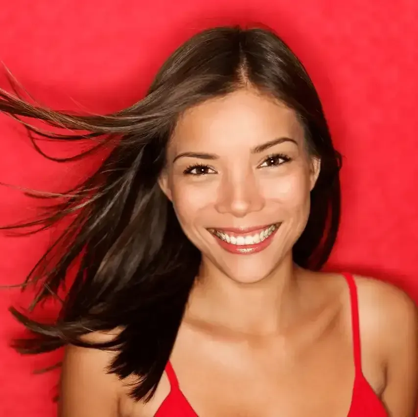 A woman in a red tank top smiles with her hair blowing in the wind
