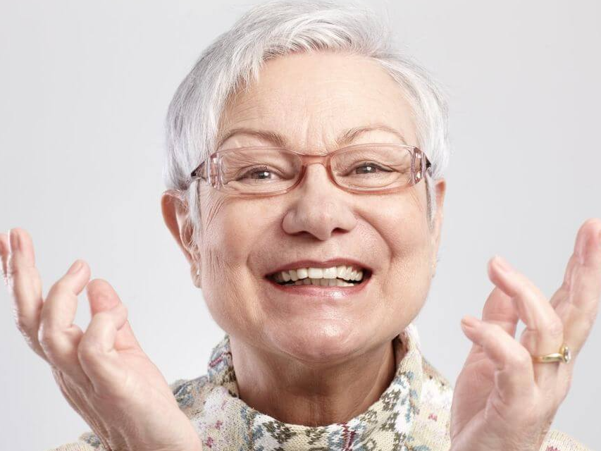 an elderly woman wearing glasses is smiling with her hands in the air