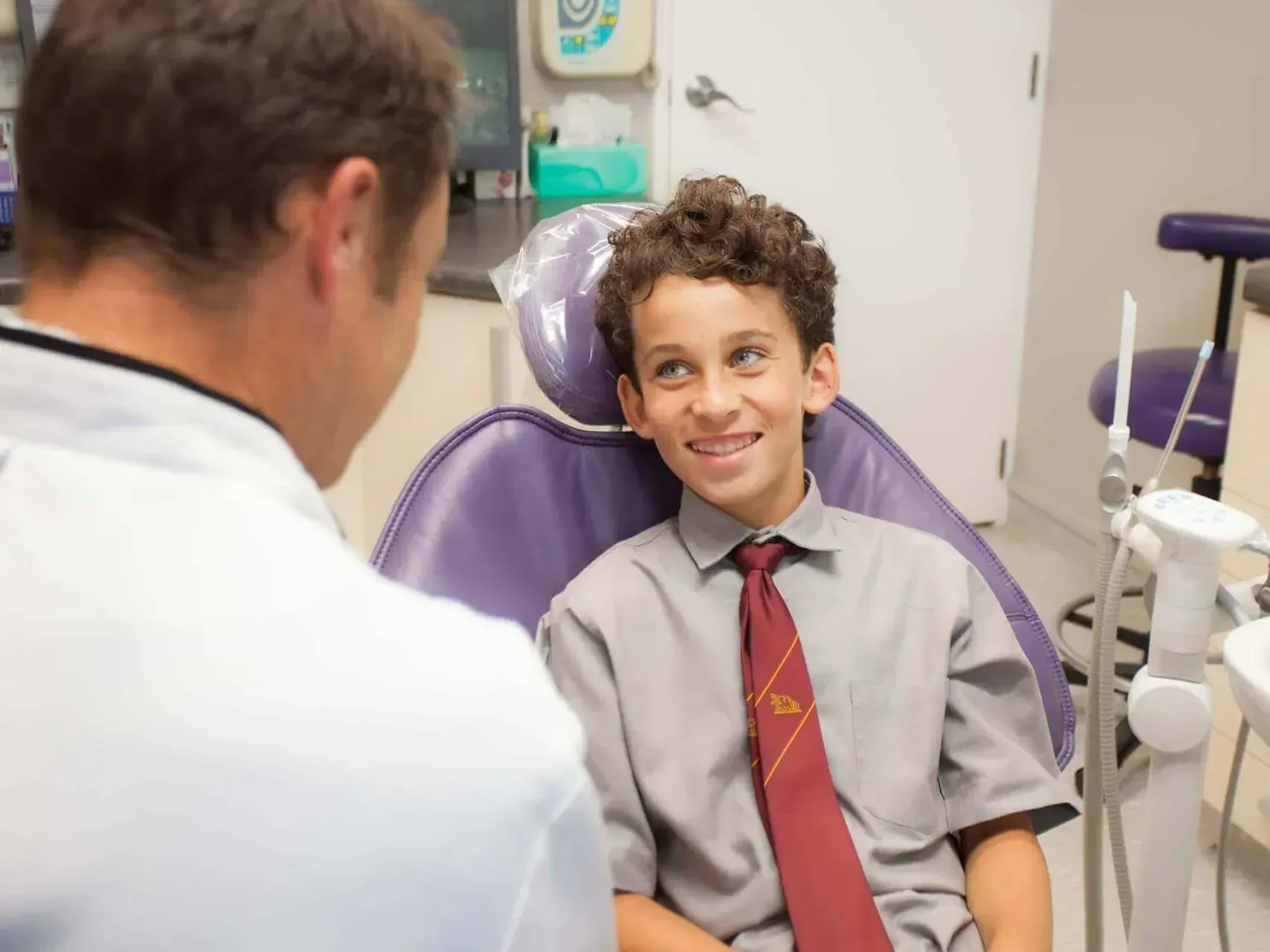 A young boy is sitting in a dental chair talking to a dentist