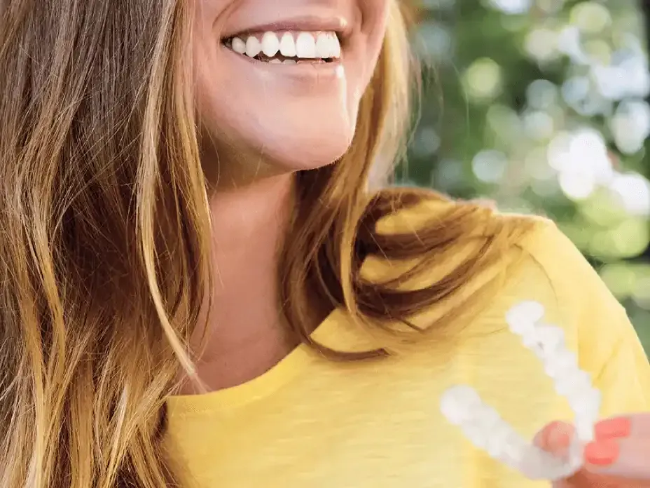 a woman in a yellow shirt is smiling and holding a clear retainer .