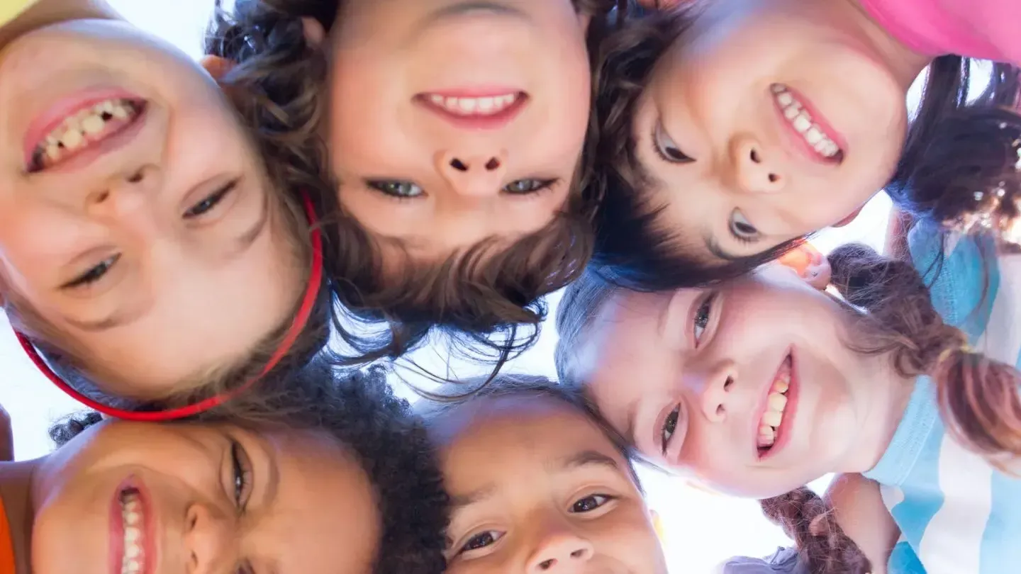 Six children smiling and looking down, close-up, outdoors.
