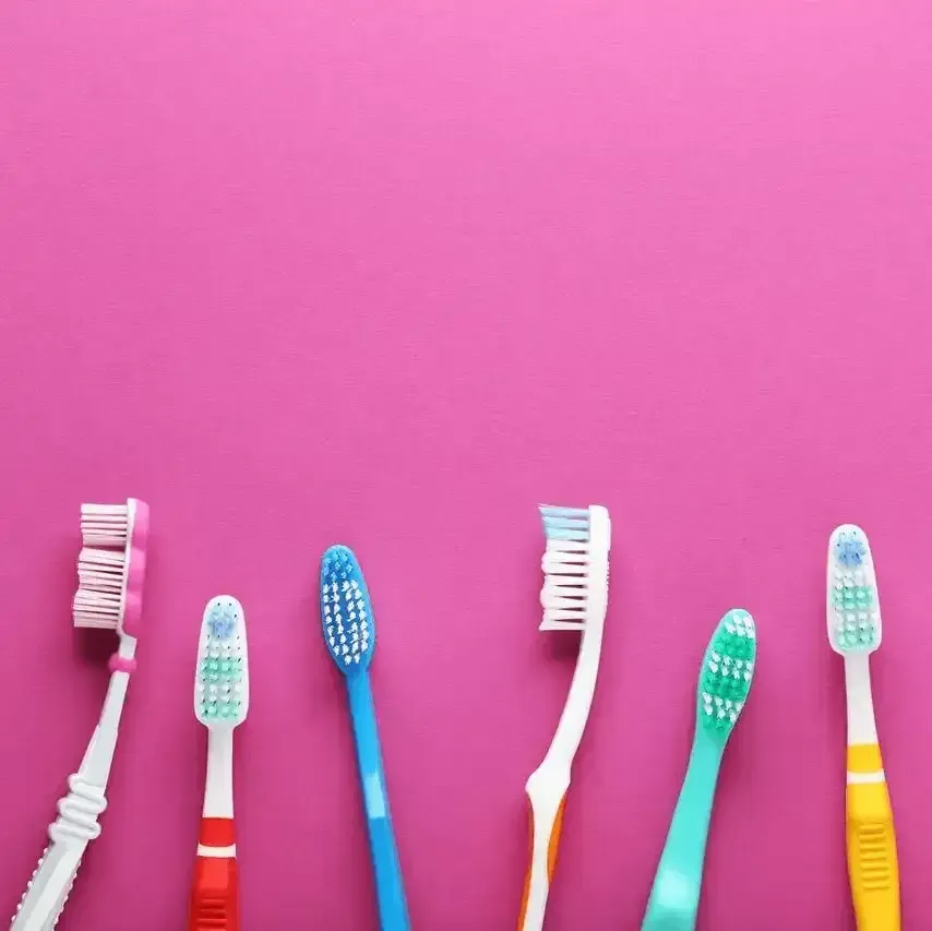 A row of colorful toothbrushes on a pink background