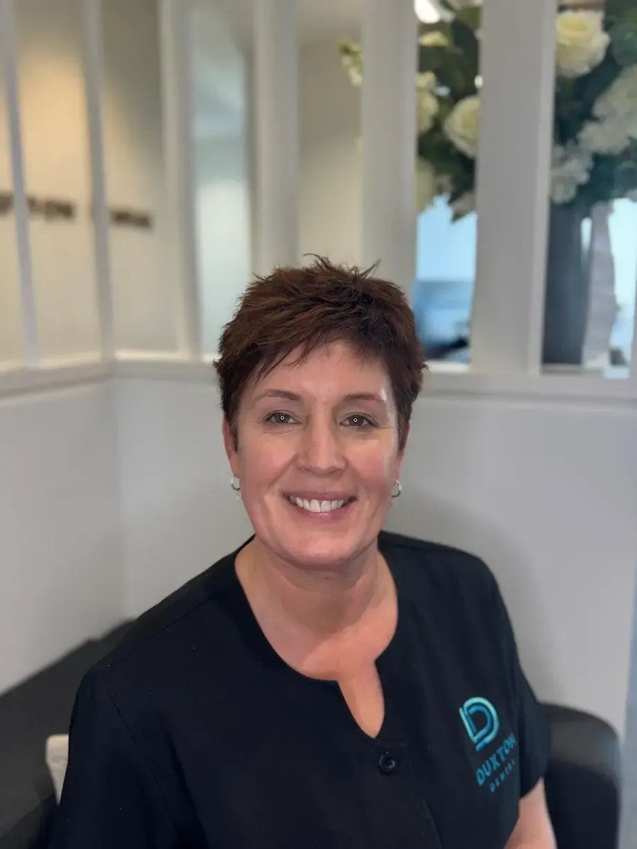 A woman wearing a black shirt and earrings is smiling in a black and white photo.