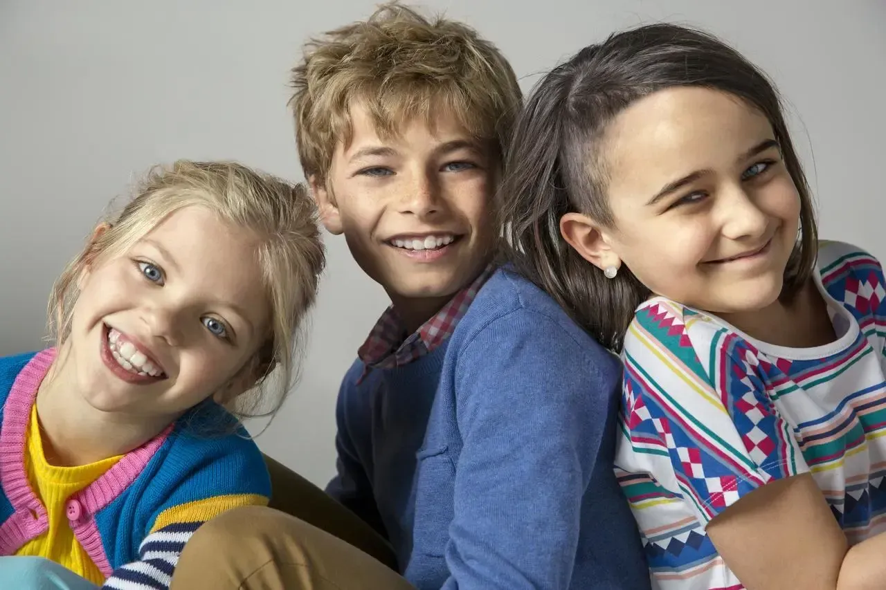 Three children are sitting next to each other and smiling for the camera.