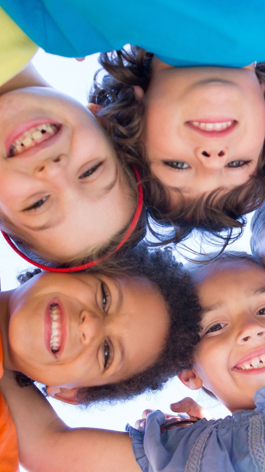 Four children smiling and looking down, faces close together.