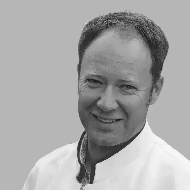 a man in a white coat is smiling in a black and white photo .