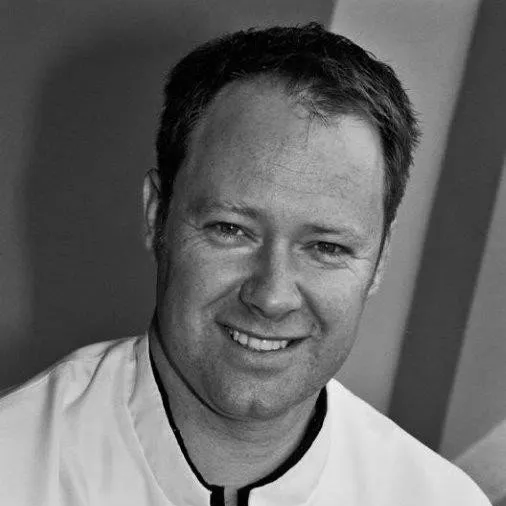 a man in a white shirt is smiling in a black and white photo .