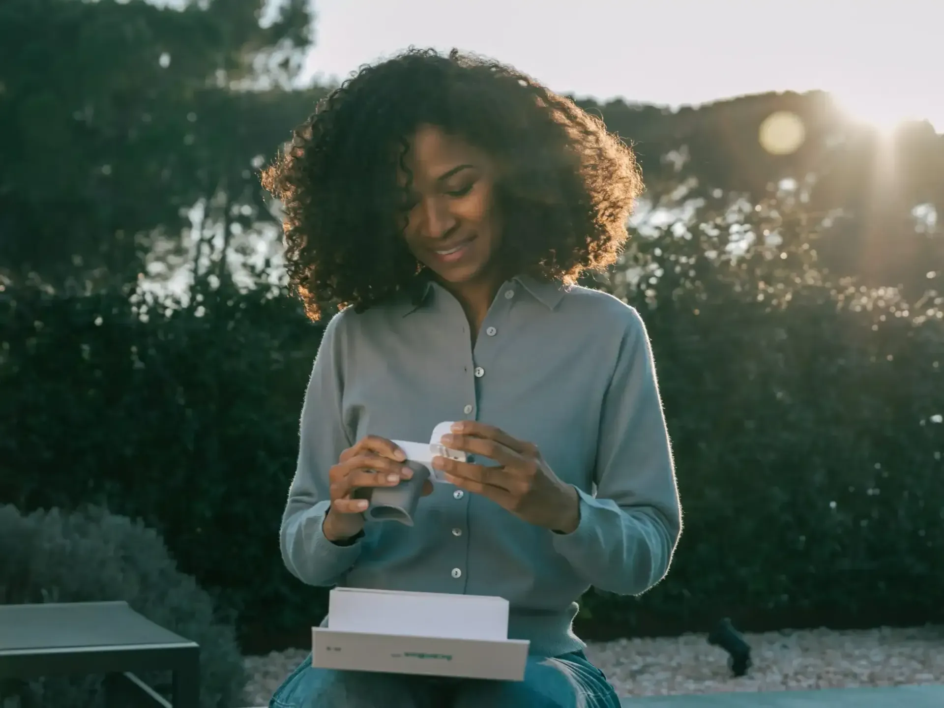 A woman is sitting on a bench holding a scanbox pro and smiling.