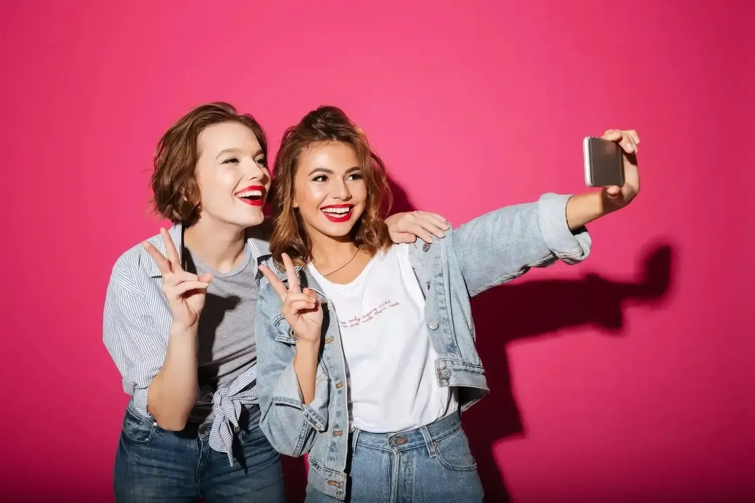 2 Girls taking a selfie showing their white teeth with a pink background