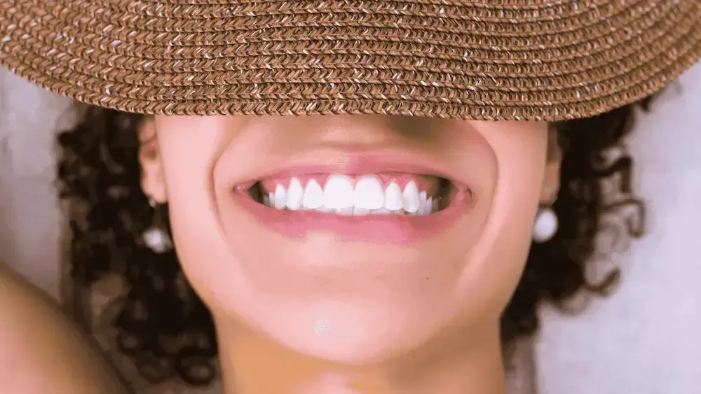 Woman with a wide smile, bright white teeth, wearing a straw hat, lying down.