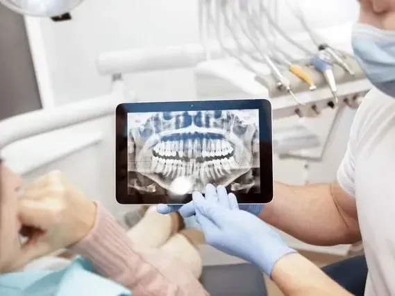 A dentist is looking at an x-ray of a patient 's teeth on a tablet.