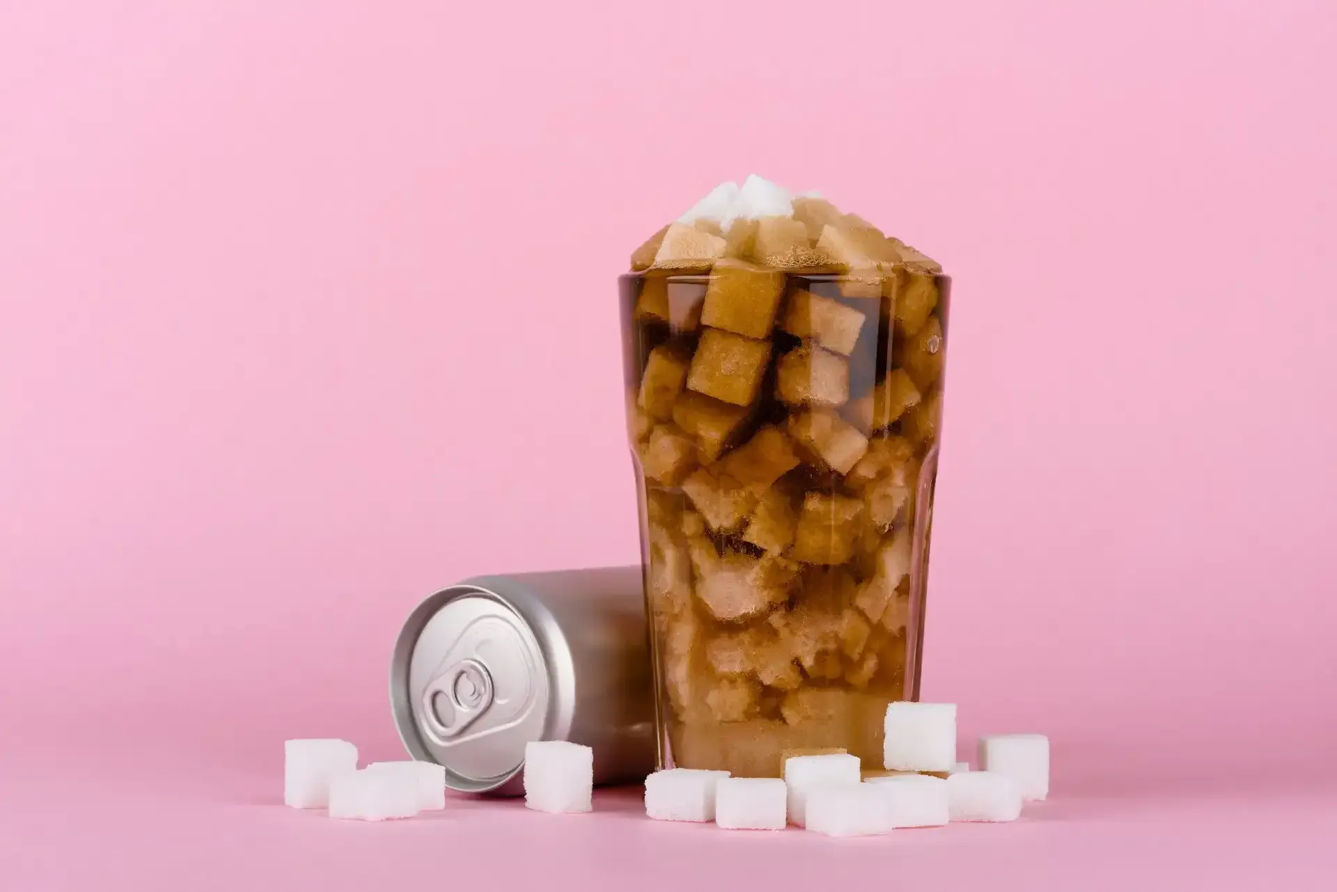 a can of soda and a glass of soda with ice cubes on a pink background .