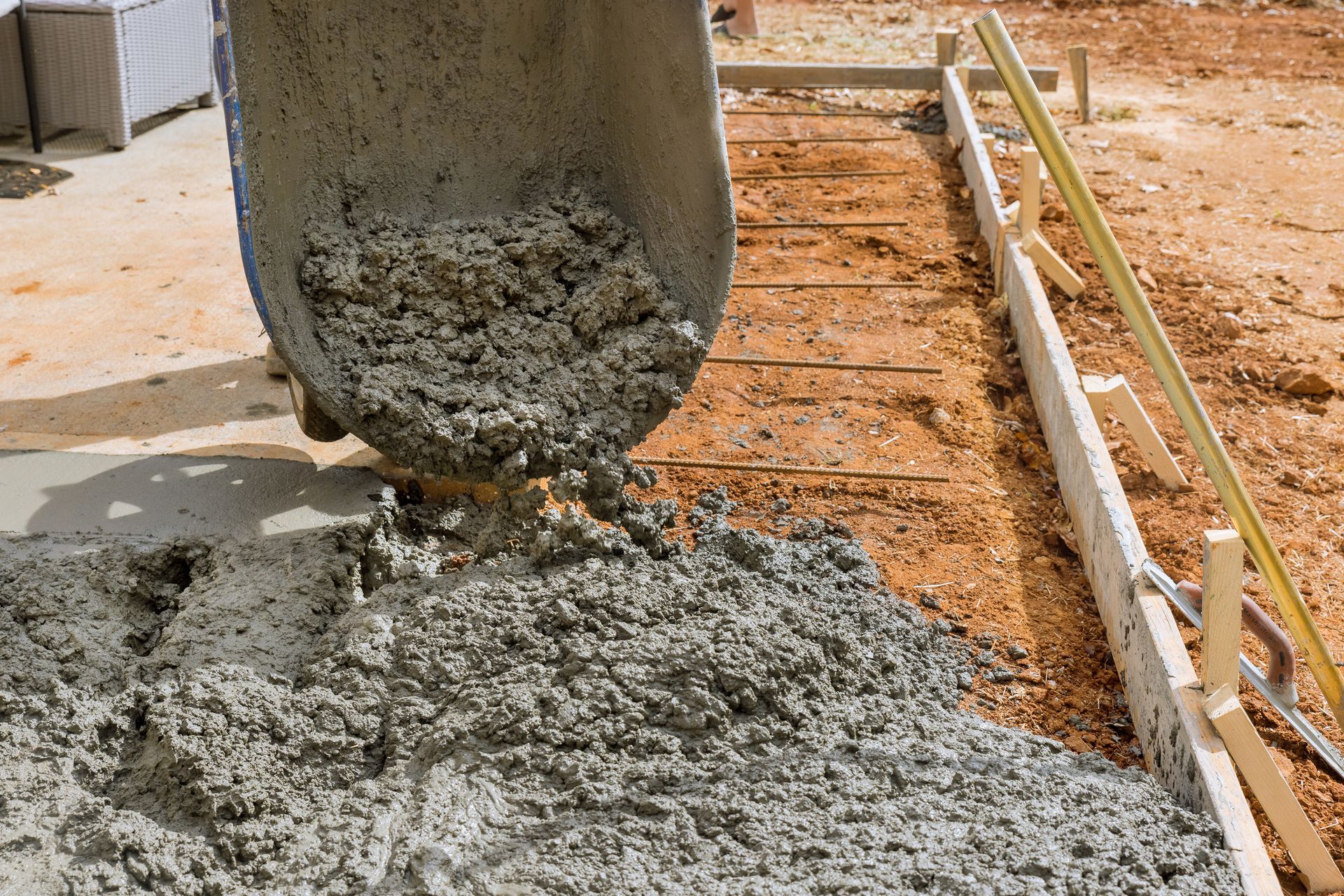 Wet concrete being poured on construction ground with orange dirt.