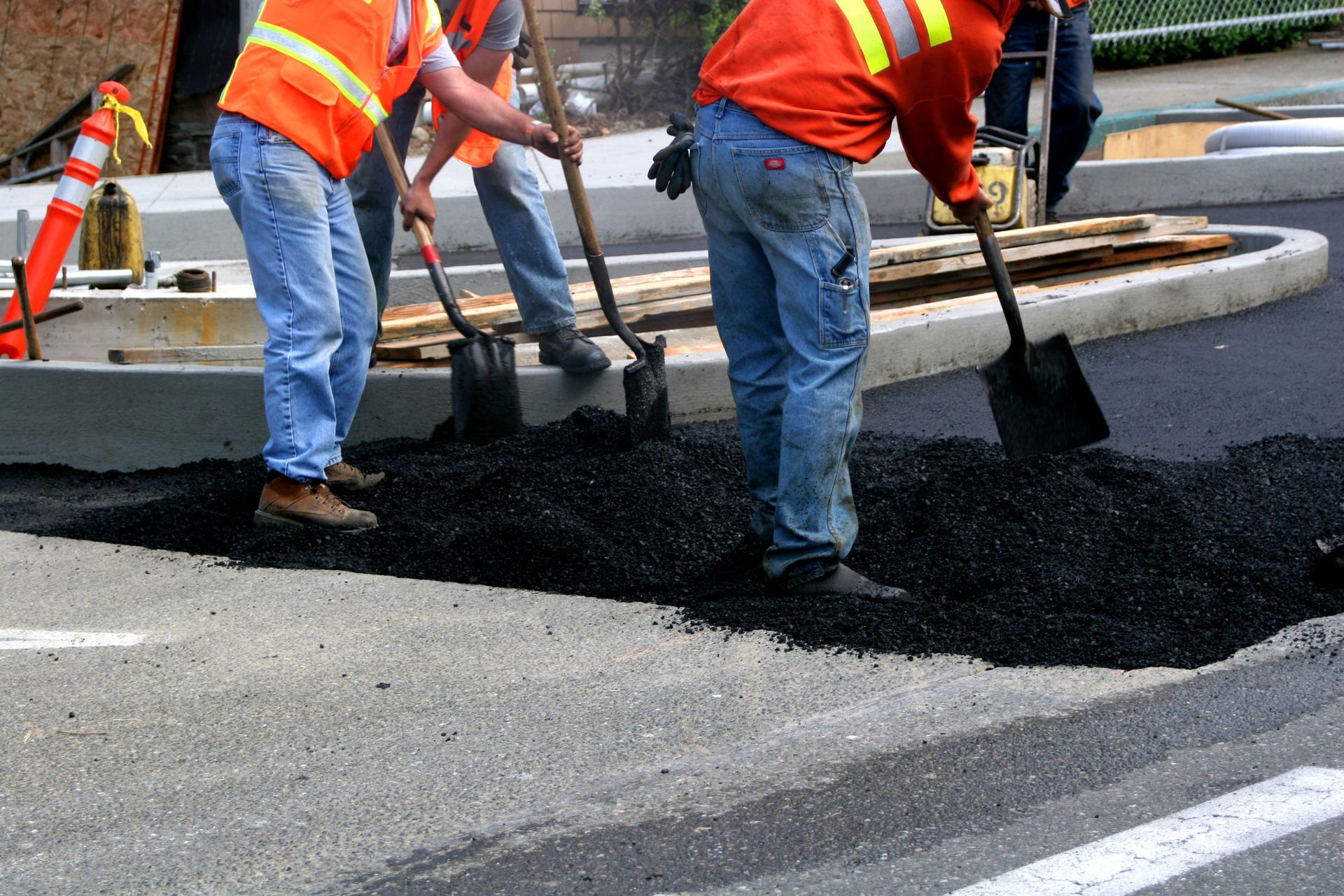 Workers wearing jeans shoveling asphalt over older pavement.