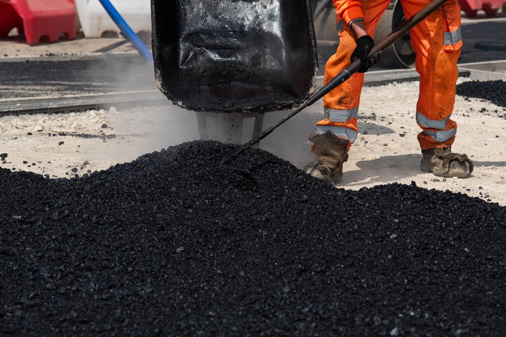Worker spreading hot asphalt on road during paving process.
