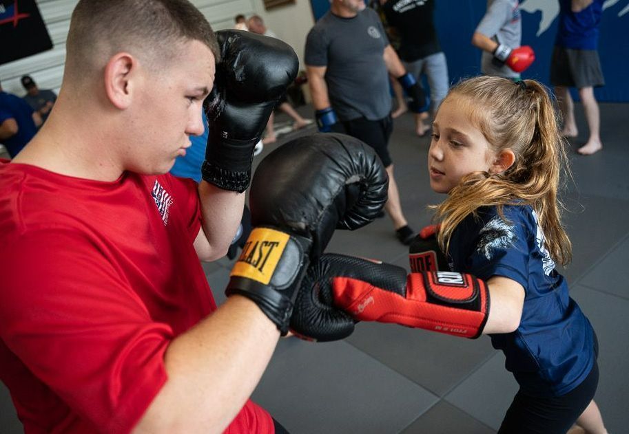 Boy in red shirt and girl in blue shirt boxing in a gym; others in background.