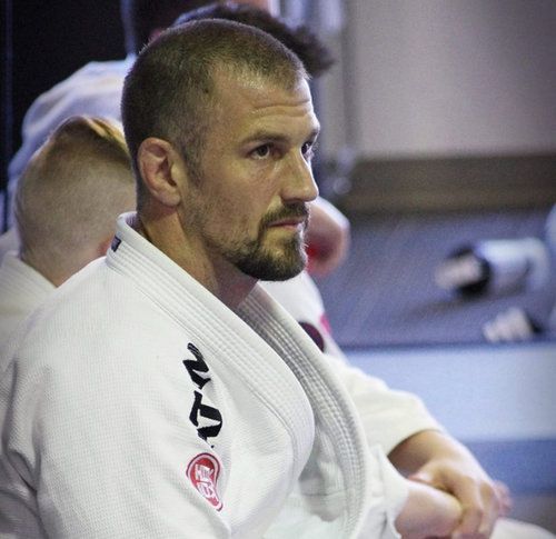 Man in white gi, short hair, serious expression, seated, training session.