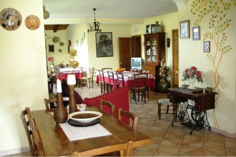 Una sala da pranzo rustica con un tavolo di legno in primo piano e una zona pranzo con un tavolo apparecchiato con una tovaglia rossa sullo sfondo.