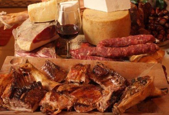 Un assortimento di formaggi, salumi, insaccati e arrosti su un tagliere di legno, accompagnato da un bicchiere di vino rosso.