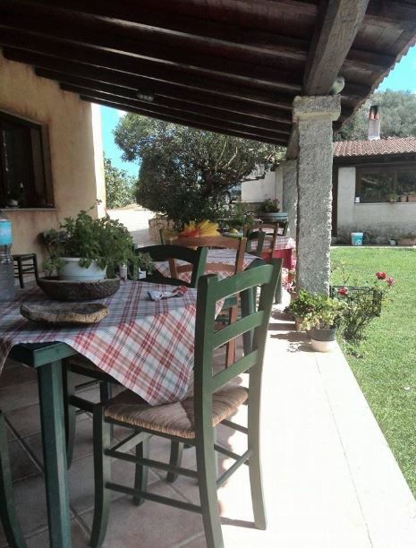 Un tavolo da patio con una tovaglia a quadri e sedie di legno verdi, sistemato sotto una veranda coperta con vista su un prato.