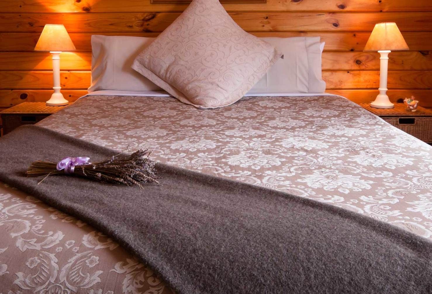 Una camera da letto accogliente con un letto con copriletto a fantasia floreale, una coperta scura, un cuscino decorativo e due lampade.