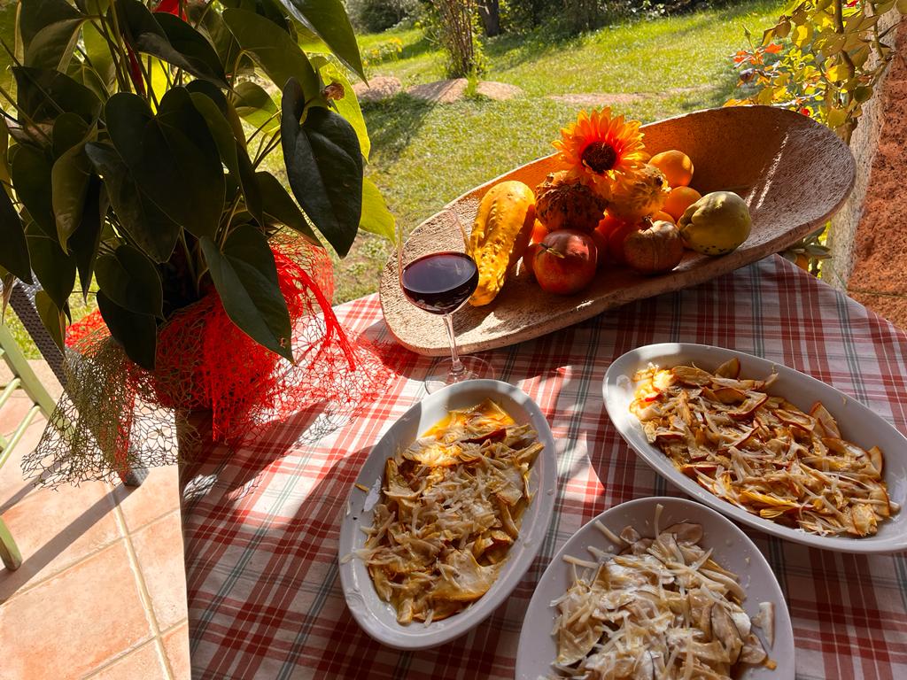 Un grande gregge di pecore bianche pascola su un pendio erboso e arido punteggiato di alberi verdi, sotto un cielo limpido e soleggiato.