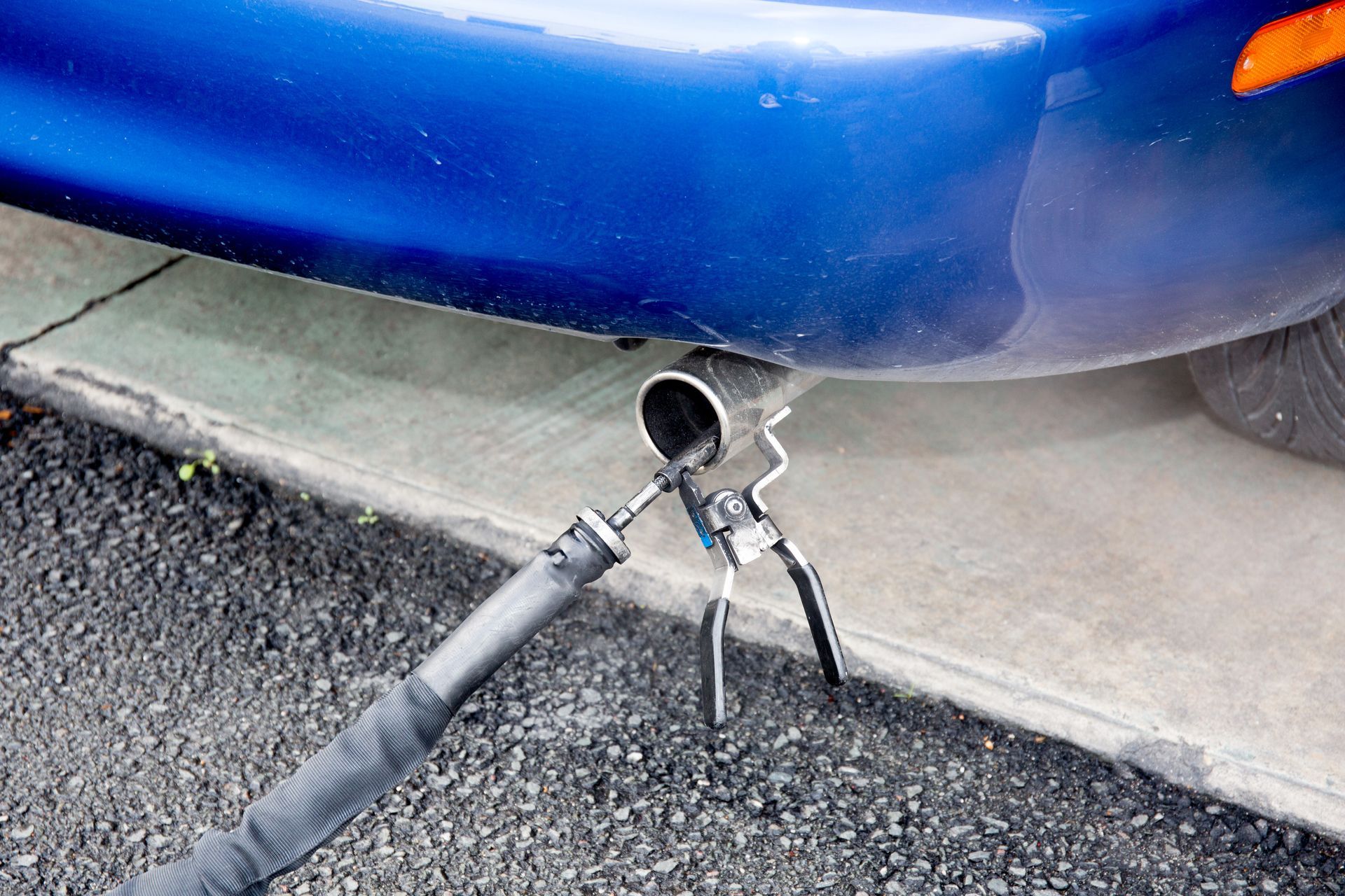 The exhaust pipe of a blue car is connected to a vacuum cleaner.