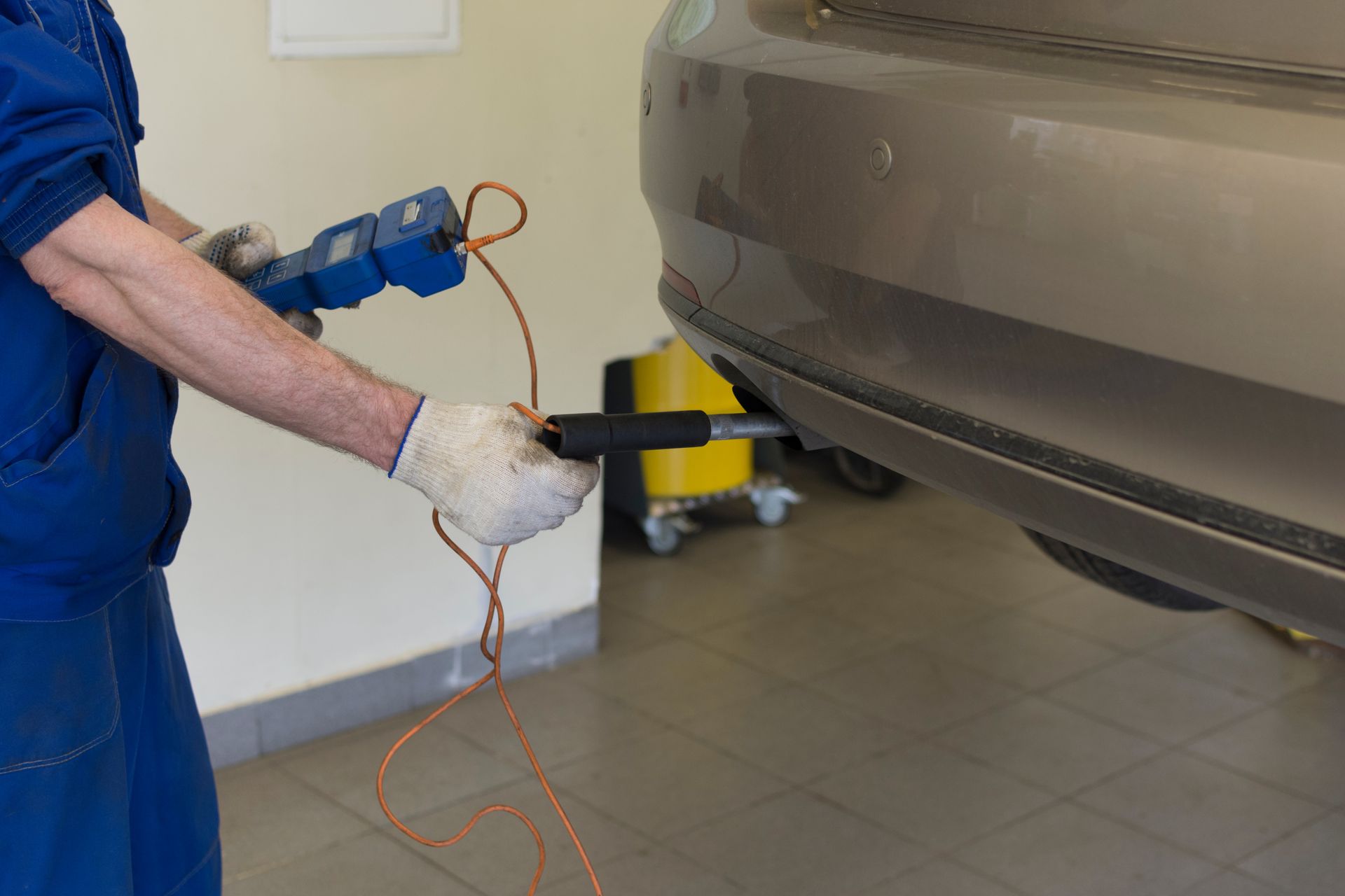 A man is holding a tool next to a car in a garage.