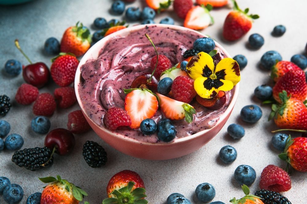 Berry smoothie bowl topped with fresh berries and an edible flower.