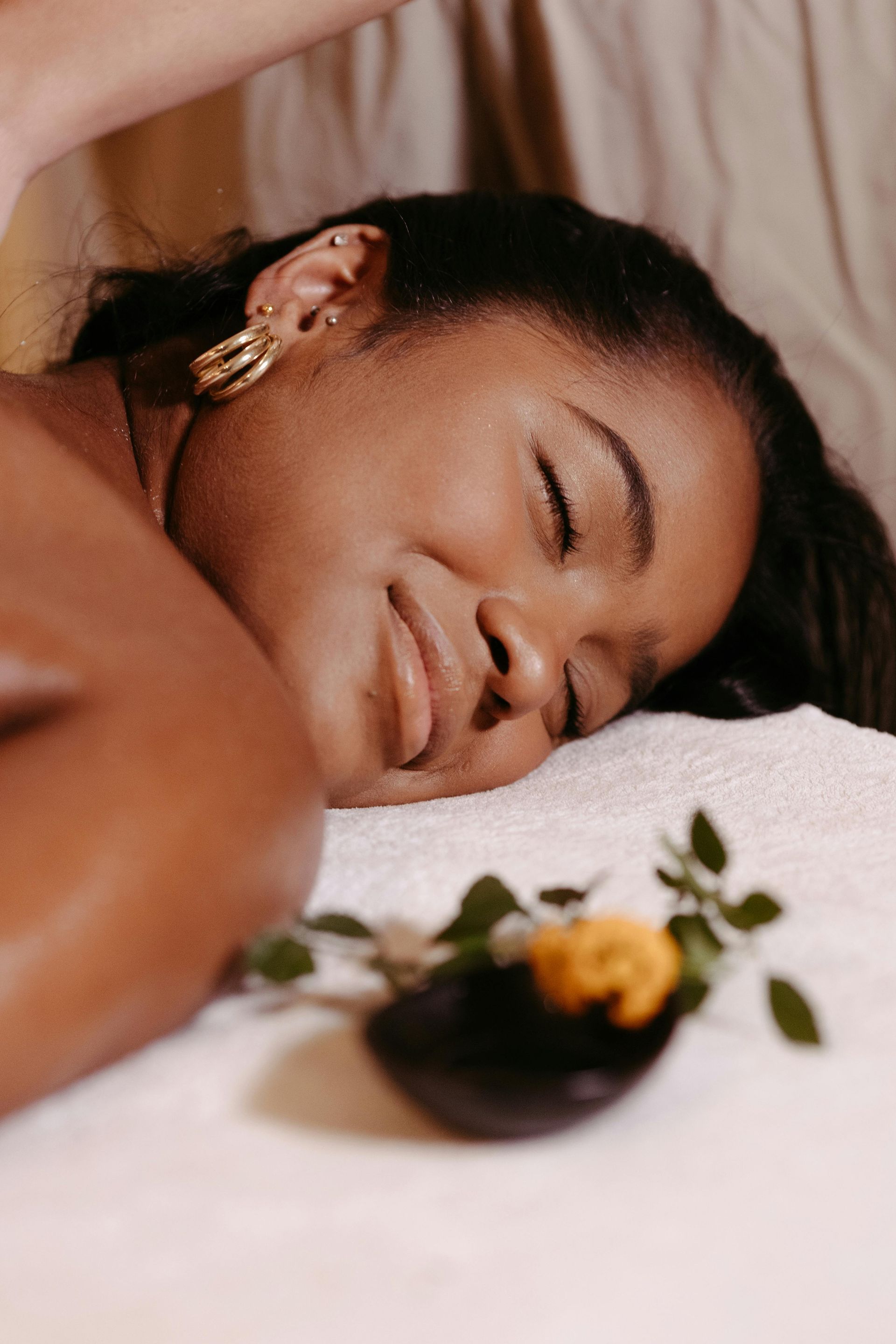 Woman receiving a massage, eyes closed, smiling, lying on white towel with flowers.