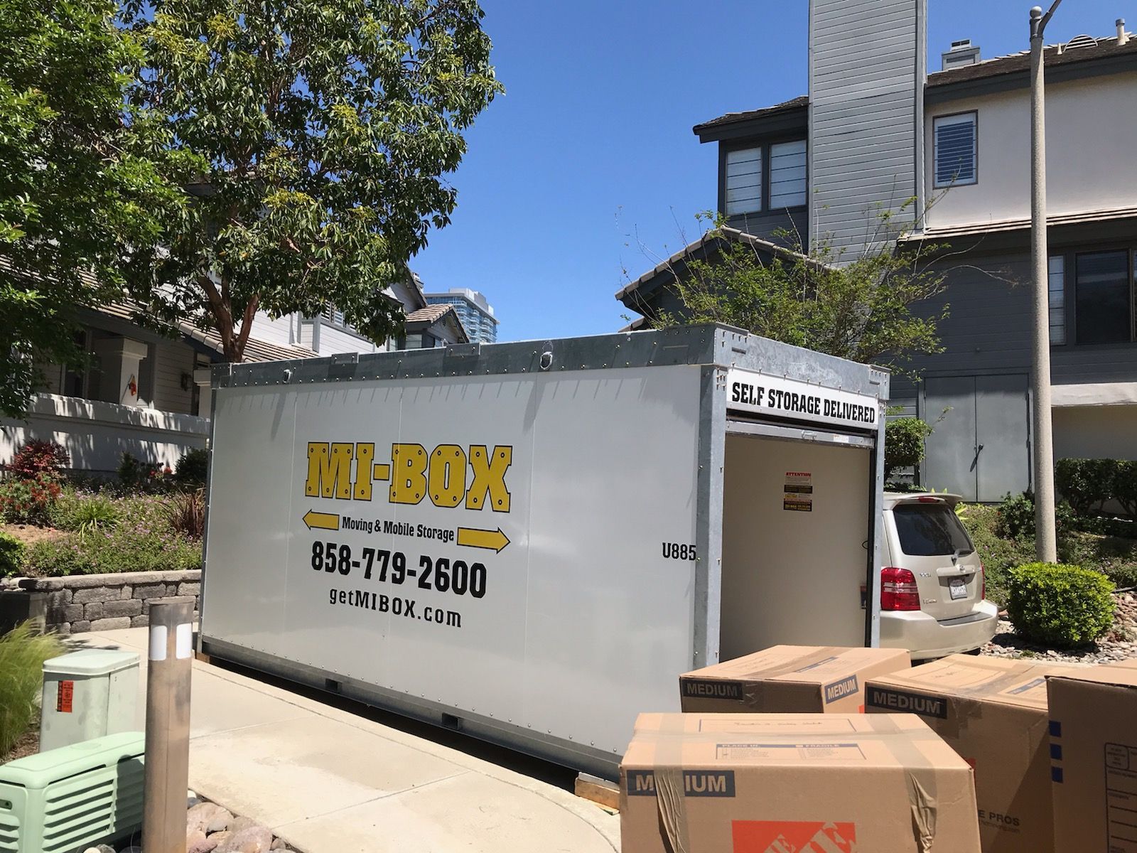 A white portable storage container is parked in front of a house.