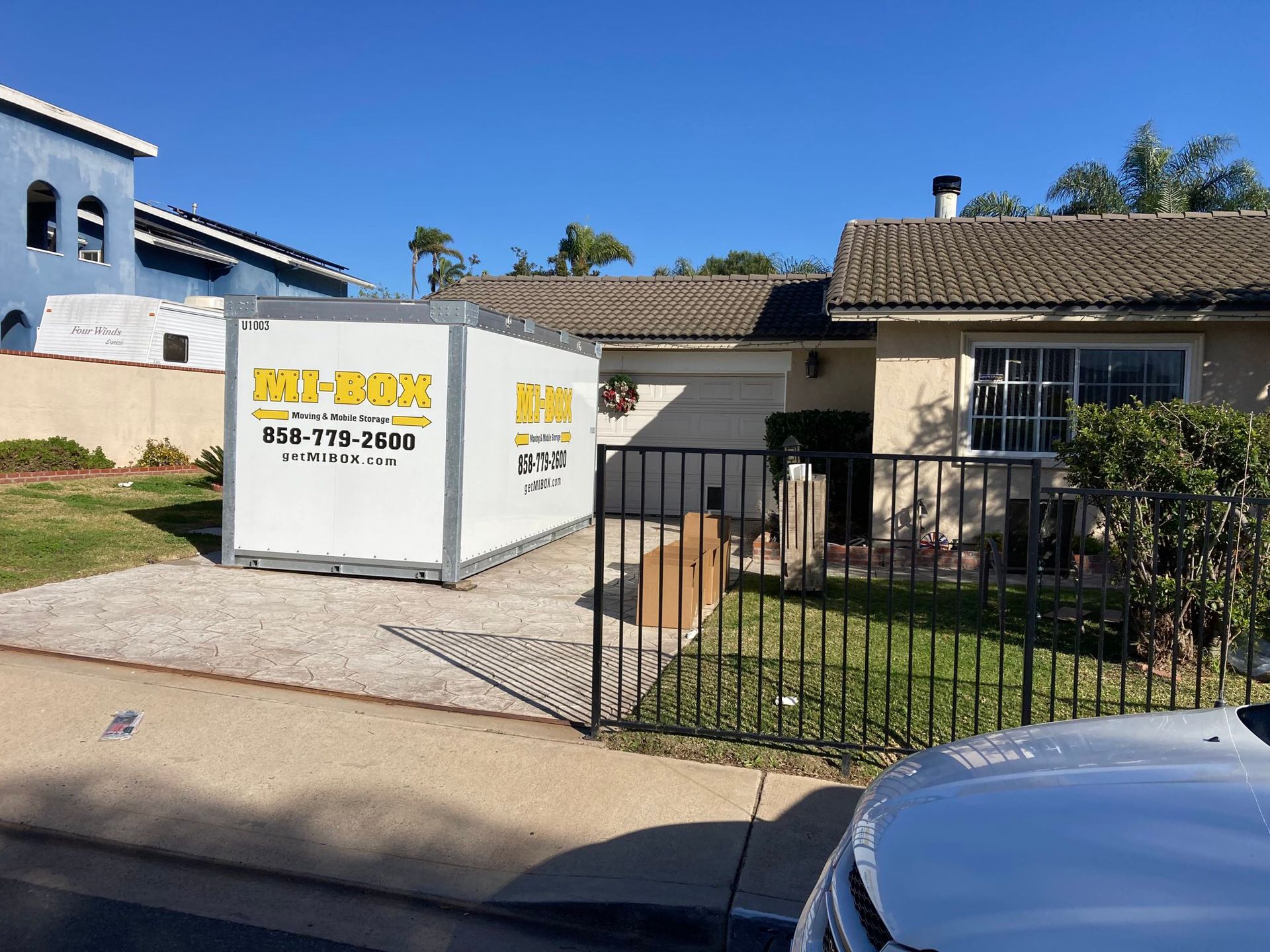 A white shipping container is parked in front of a house.