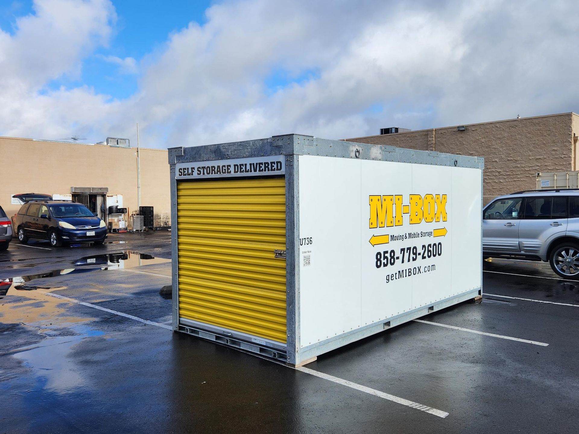 A white portable storage container with a yellow door is in a parking lot.