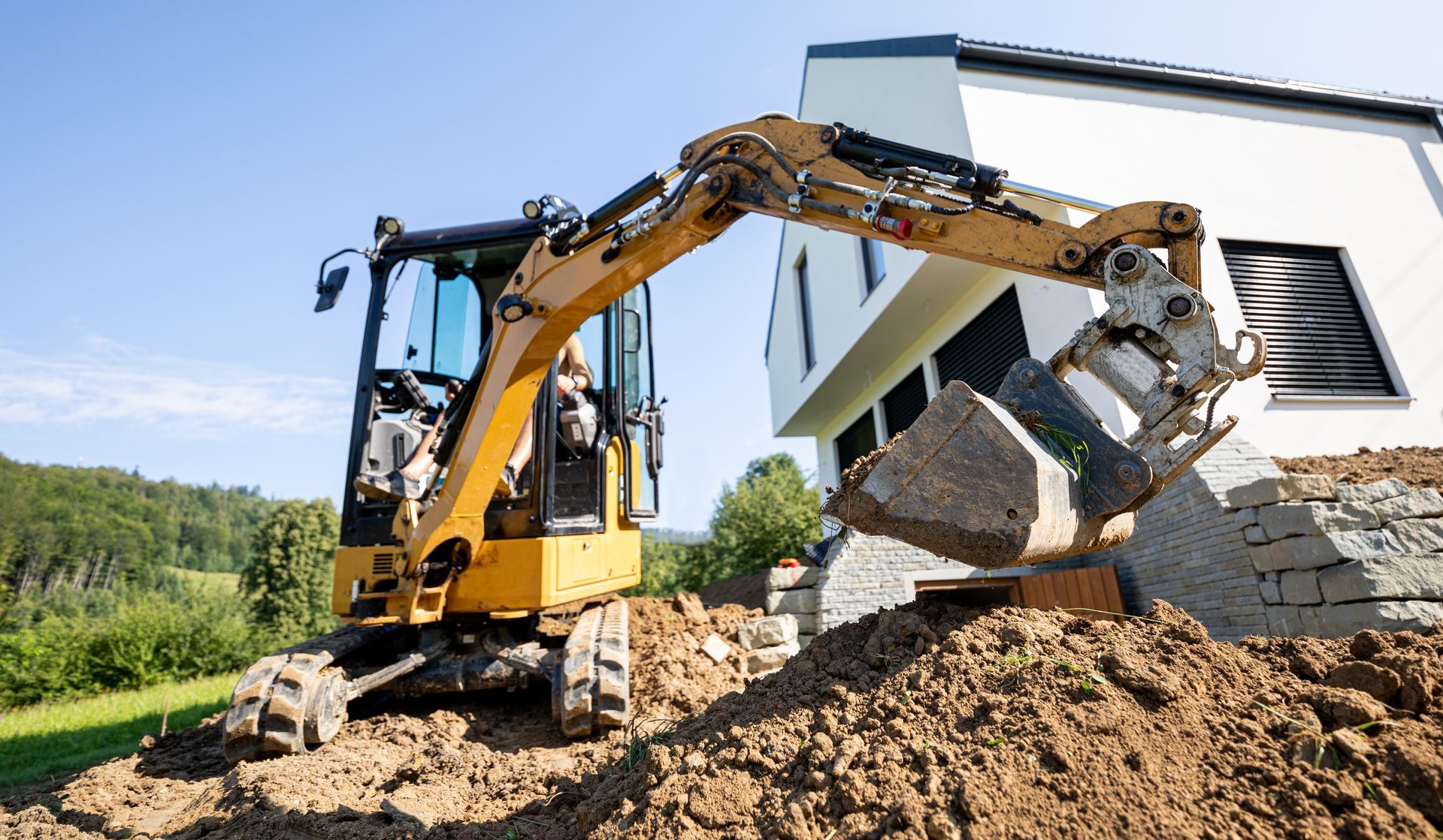 Une petite excavatrice charge de la terre dans un tas devant une maison.