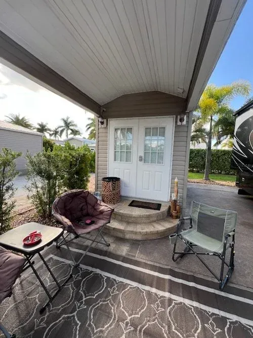 RV site with a small white building, outdoor seating, and palm trees.
