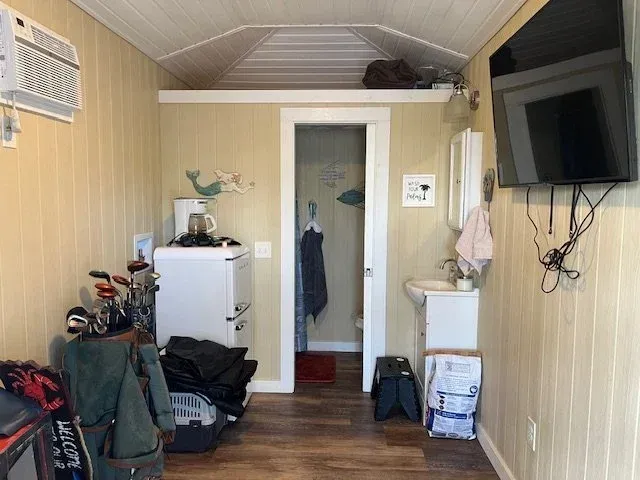 Small room with golf clubs, mini-fridge, doorway to bathroom, mounted TV, and air conditioner.