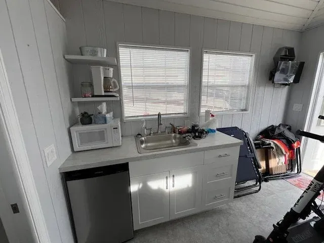 Small kitchen area with a sink, microwave, and refrigerator under a window.