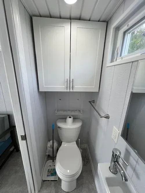 Small bathroom with toilet, cabinet, towel rack, and sink. White walls, light fixture, small window.