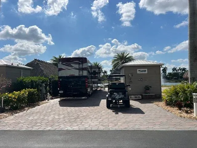 RV parked in a brick driveway with a golf cart in front of a house under a cloudy sky.