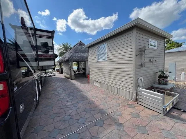 RV parked next to a small building and thatched roof gazebo on a brick-paved area under a blue sky.