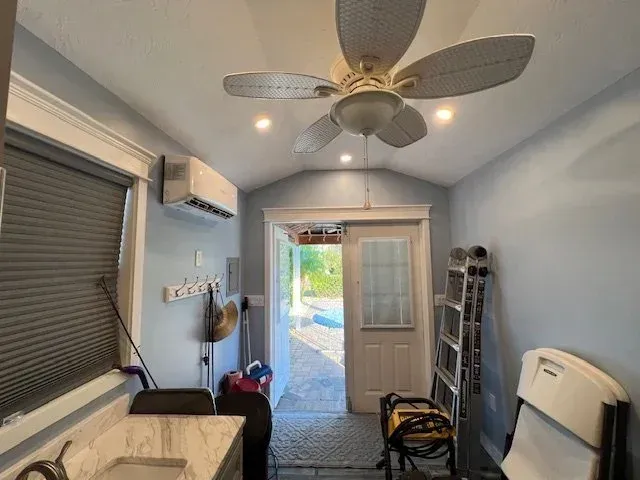 Small blue room with open door to outside, ceiling fan, air conditioning, and work equipment.