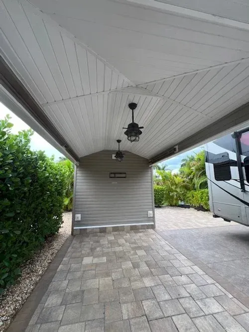 Covered RV parking, gray siding, paver driveway, two ceiling fans.