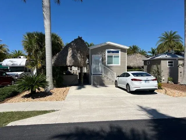 A small beachside home with a white car in the driveway. Palm trees and a clear blue sky.