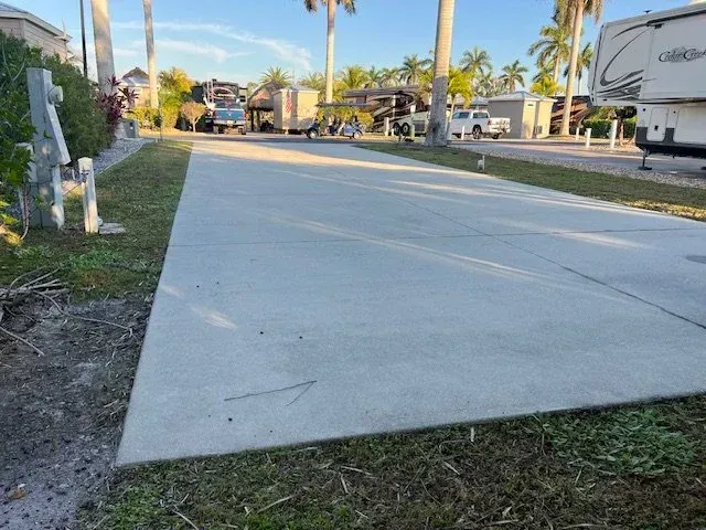 Concrete RV pad with grassy border, several RVs and palm trees in a campground.
