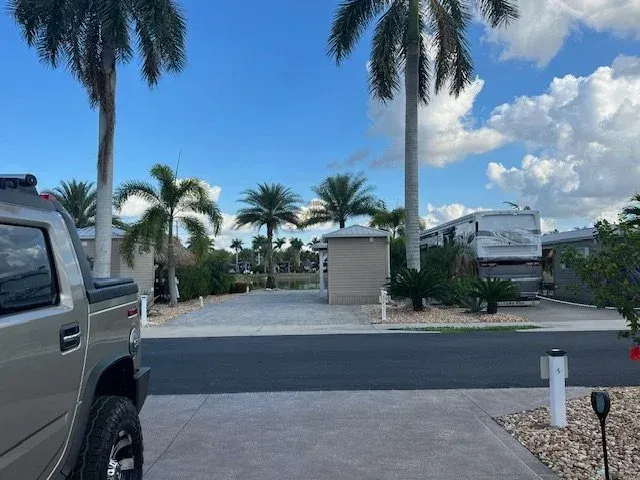 A silver Hummer parked on a driveway in a tropical RV park under a blue sky, palm trees.