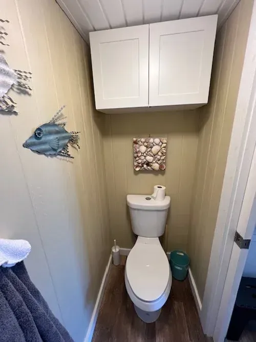Small bathroom with a toilet, a white cabinet, and wall decorations.