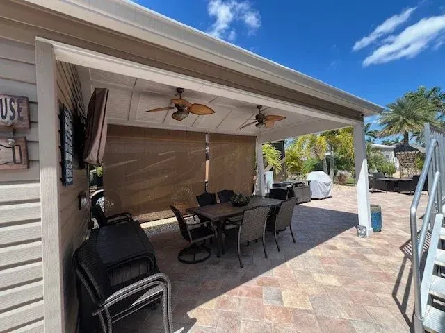 Outdoor dining area with a table, chairs, and ceiling fans. Beige and brown tones, sunny day.